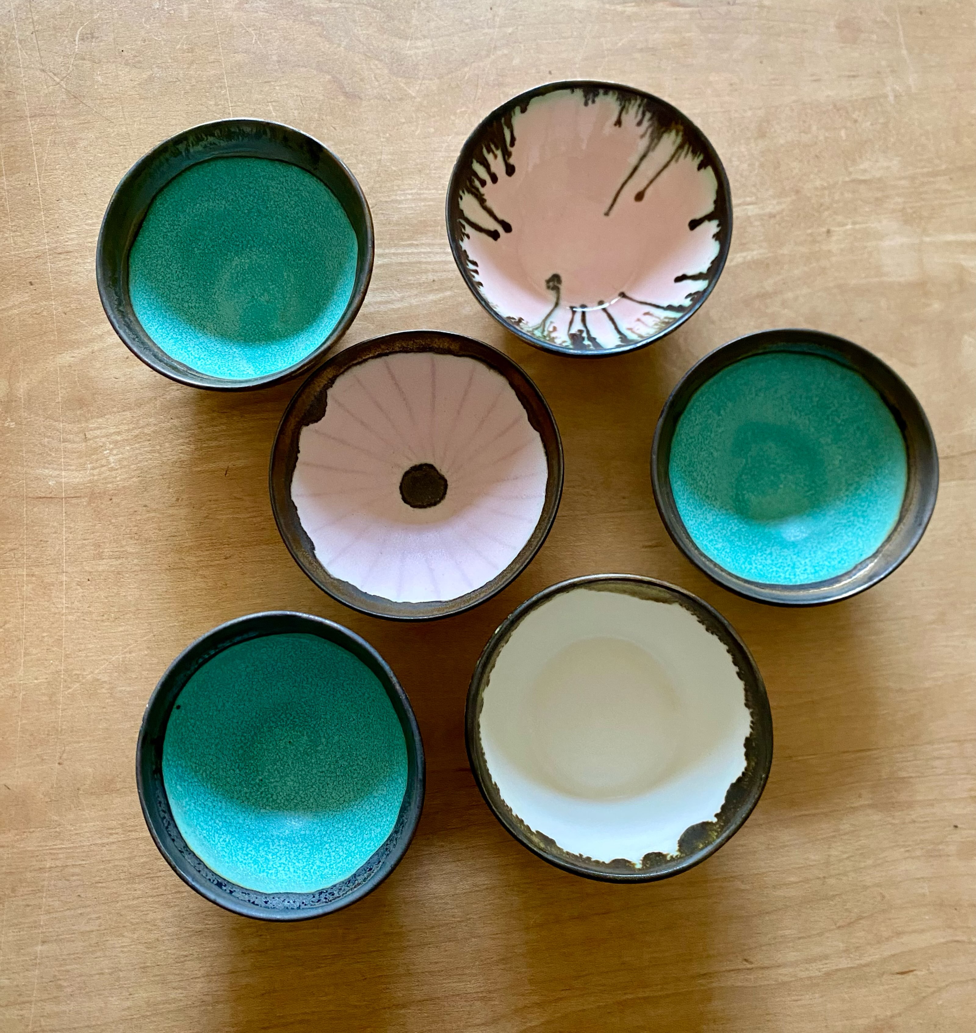 Small test bowls trying out different bronze glaze recipes with various matt and glossy glazes inspired by Lucie Rie and Emmanuel Cooper. The fluidity depends on the bronze glaze recipe and application thickness as well as the glaze underneath. Fired to cone 8 in an electric kiln, the recipes are in my book Special Effect Glazes.